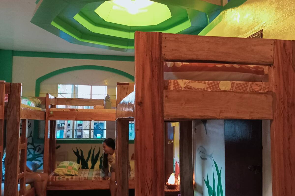 Una habitación con literas, una decoración en tonos verde y blanco, y un diseño de techo original.