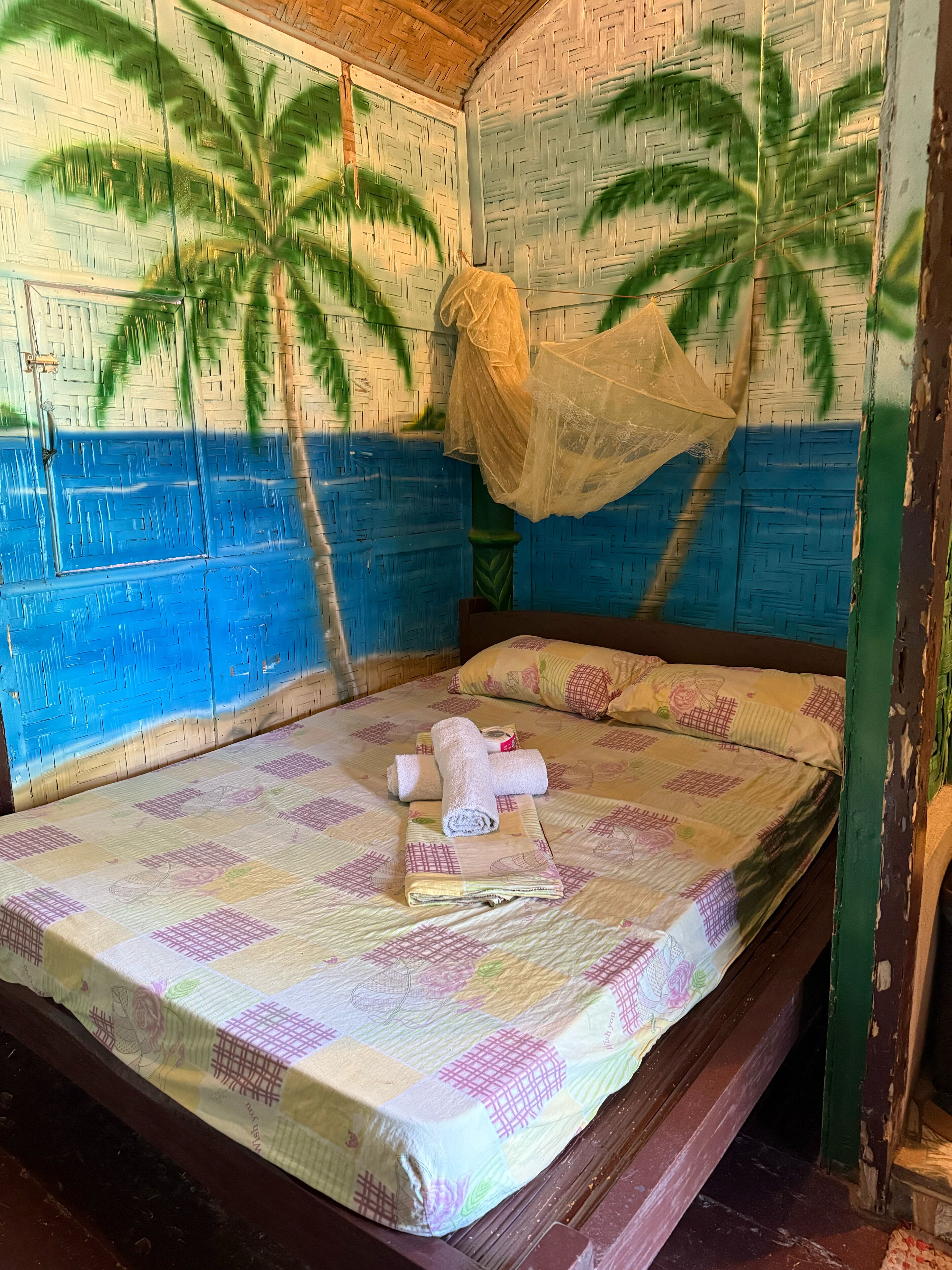 A room with a bed, a hanging mosquito net, and a wall with a palm tree pattern.