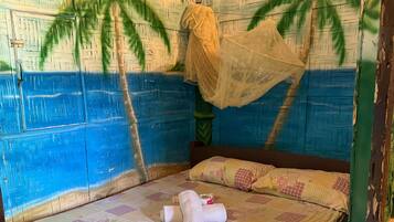 A room with a bed, a hanging mosquito net, and a wall with a palm tree pattern.