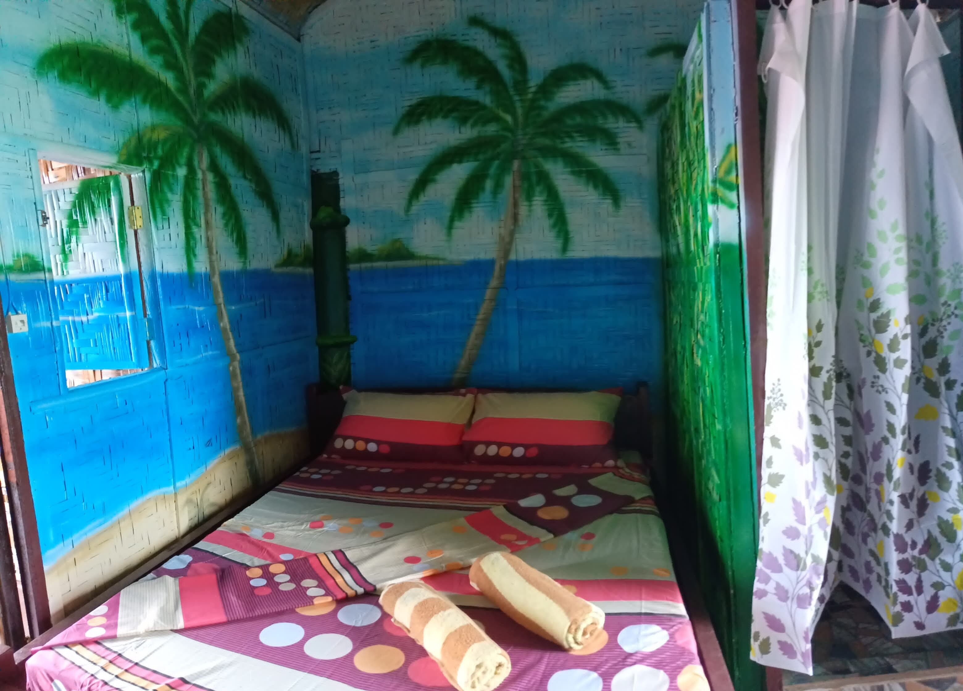 Ein Zimmer mit einem Bett, einem Fenster und einer Wandmalerei von Palmen.