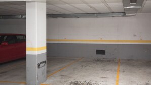 Een parkeergarage met betonnen vloeren, gele parkeerlijnen en een rode auto op de achtergrond.