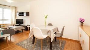 Een moderne eetruimte met een ronde tafel, witte stoelen, een kleine vaas met bloemen en een televisie op de achtergrond.