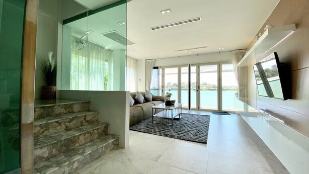 A modern living room with a staircase, a sofa, a coffee table, and a large window offering a view of the sea. - Baan Jayden Duplex Seaview Villa (Phuket)