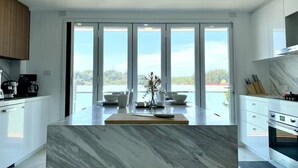 A modern kitchen with a marble island, large windows, and a view of the outdoors. - Baan Jayden Duplex Seaview Villa (Phuket)