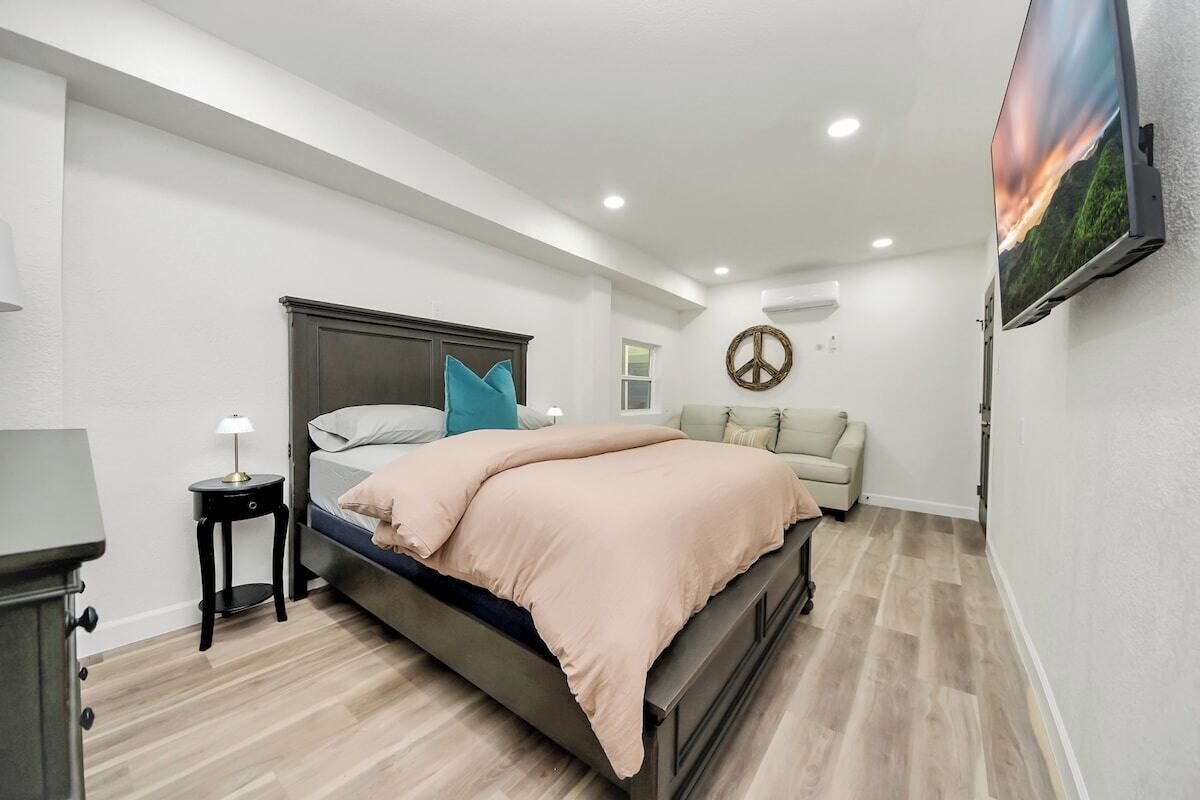 A bedroom with a bed, a bedside table, a lamp, a wall-mounted TV, and a couch.
