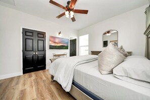 A bedroom with a bed, a ceiling fan, a door, and a painting on the wall. - Family Hub for Boardwalk Oktoberfest/Halloween Fun (Kemah)