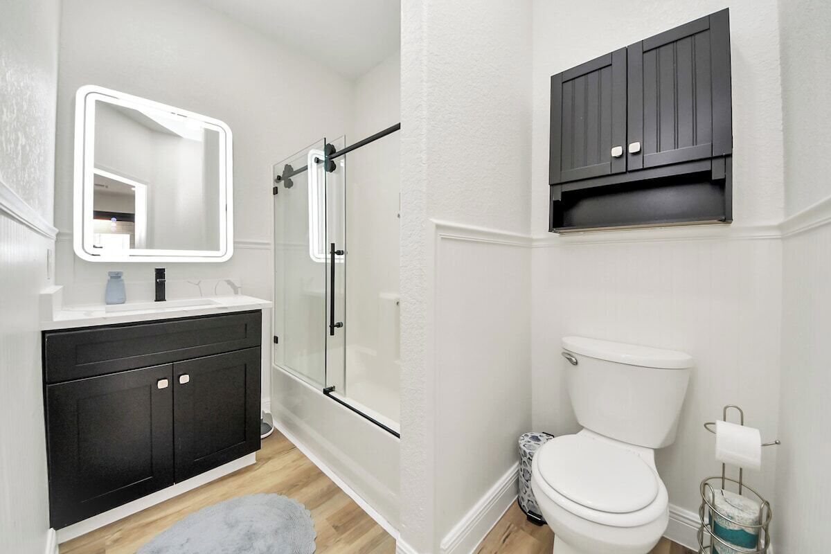 A bathroom with a white vanity, a glass shower enclosure, a white toilet, and a dark wooden cabinet above the toilet.