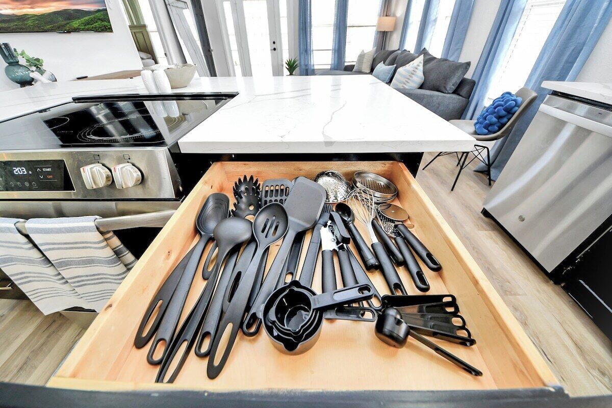 A modern kitchen with a central island, stainless steel appliances, and a variety of utensils in a drawer.