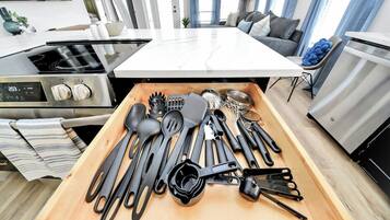 A modern kitchen with a central island, stainless steel appliances, and a variety of utensils in a drawer.