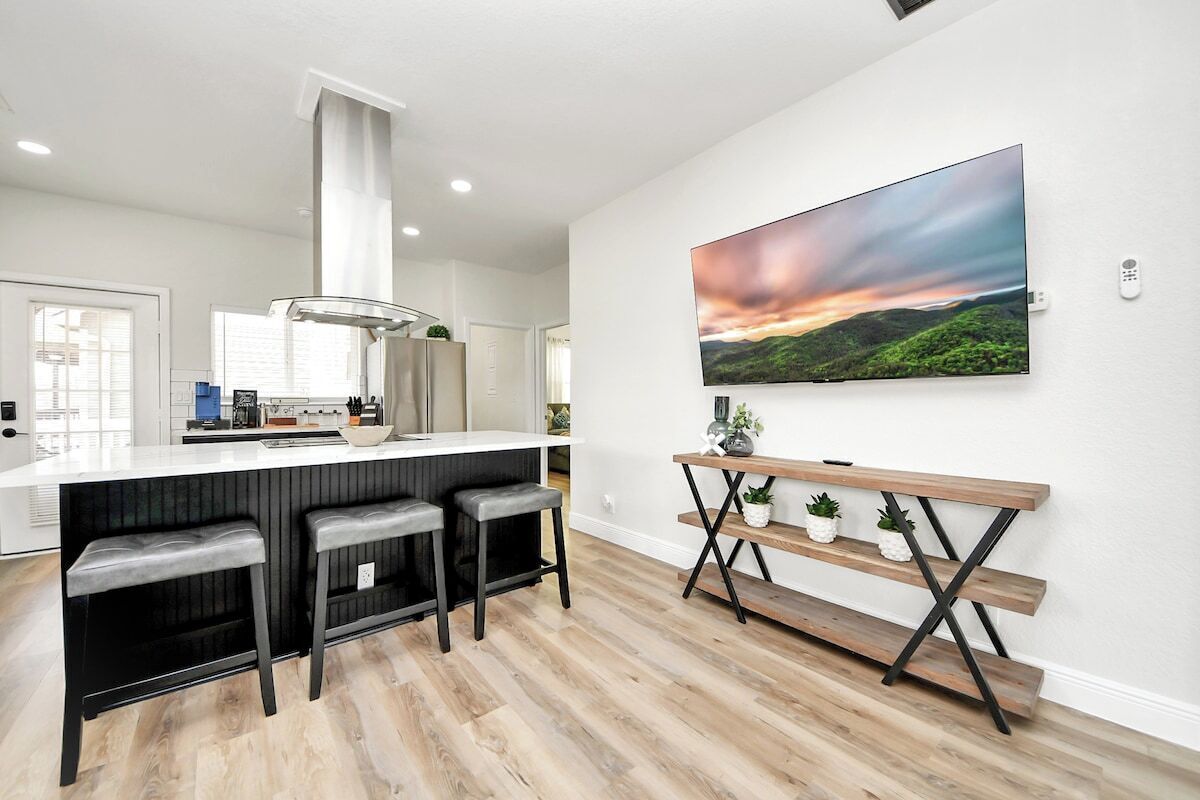 A modern kitchen with a bar area, a large TV mounted on the wall, and a wooden bench with potted plants.