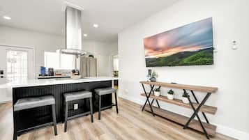 A modern kitchen with a bar area, a large TV mounted on the wall, and a wooden bench with potted plants.