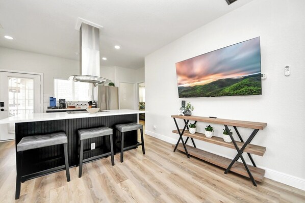 Une cuisine moderne avec un coin bar, un grand téléviseur fixé au mur et un banc en bois agrémenté de plantes en pot.