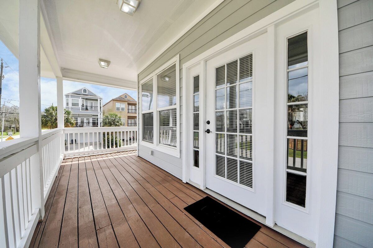 A covered porch with a wooden deck, white railings, and a black doormat.