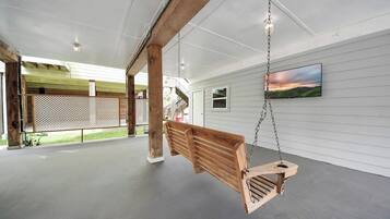 Eine hölzerne Schaukel hängt von der Decke in einem geräumigen, überdachten Bereich mit Betonboden und weißen Wänden.