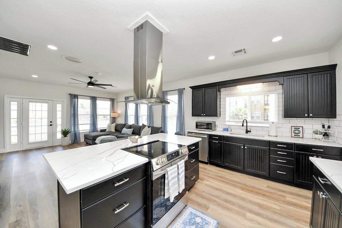 A modern kitchen with a central island, black cabinetry, and a large window.