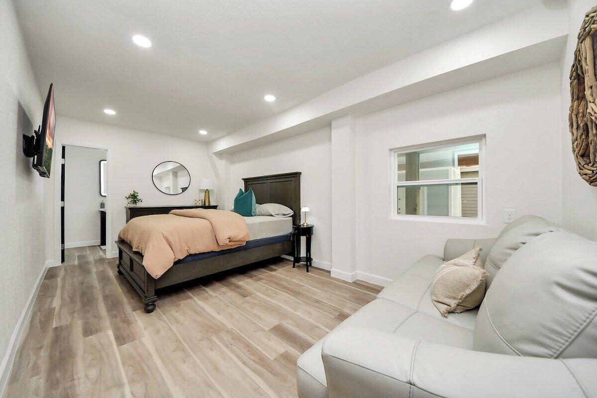 A bedroom with a bed, a bedside table, a mirror, a window, and a sofa.