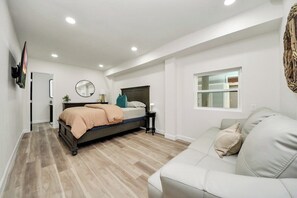 A bedroom with a bed, a bedside table, a mirror, a window, and a sofa.
