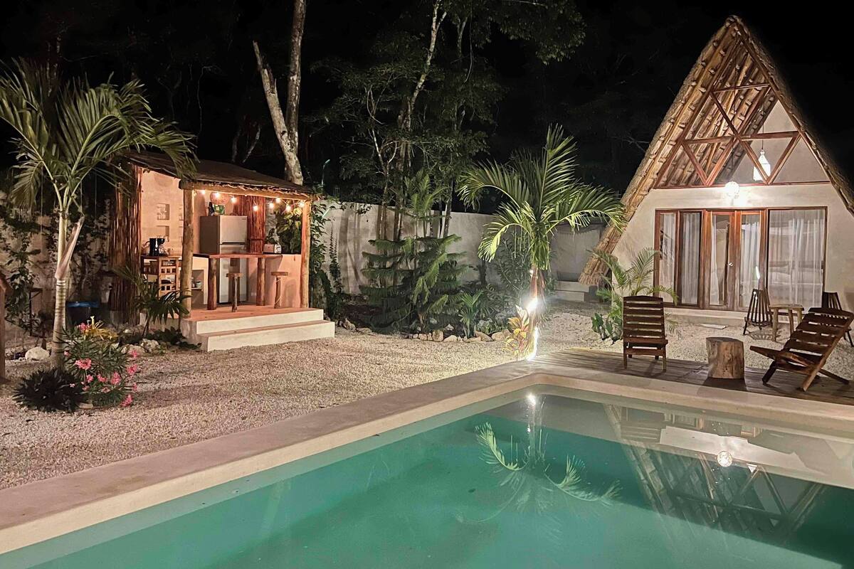 Un espace piscine agrémenté d’un petit bar et d’un coin salon, entouré de plantes tropicales et bordé d’un bâtiment à toit de chaume.