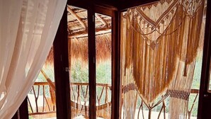 Una habitación con cama, vista a un espacio exterior con terraza de madera y techo de paja.