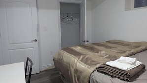 A small, neatly organized bedroom with a bed, a chair, and a closet with hanging clothes.