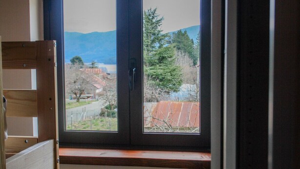 A room with a window overlooking a residential area, a wooden bench, and a door.