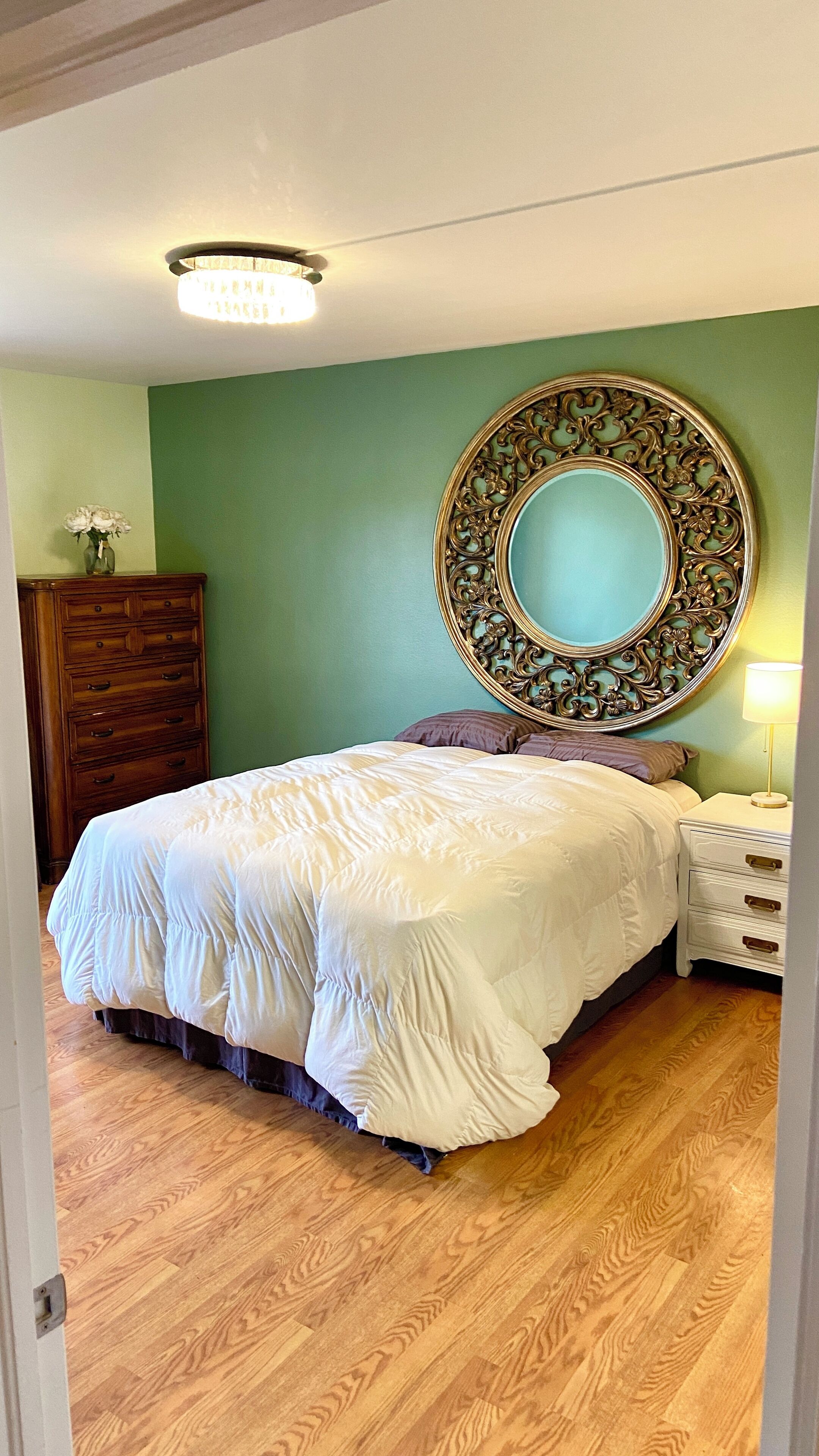 Une chambre à coucher comprenant un lit, une commode, une table de chevet et un grand miroir au mur.