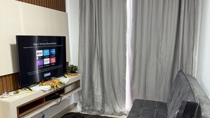 Ein modernes Wohnzimmer mit einem flachbildfernseher, der an einer Holzvertäfelung angebracht ist, einem grauen Sofa, einem schwarzen, flauschigen Teppich und einem Standventilator.