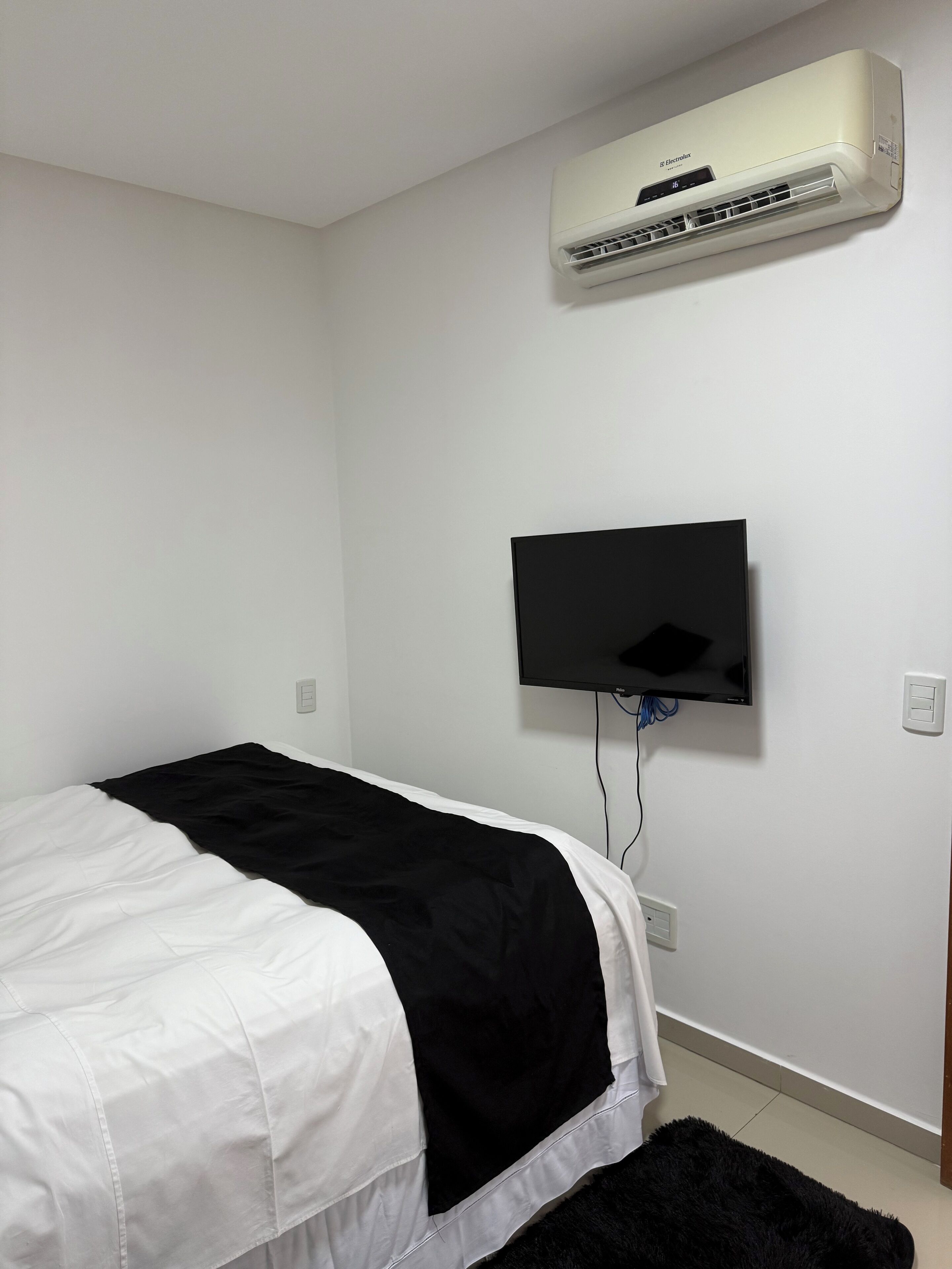 A bedroom with a bed, a mounted air conditioner, and a wall-mounted television.