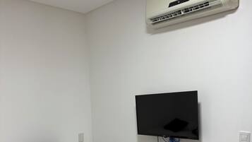 A bedroom with a bed, a mounted air conditioner, and a wall-mounted television.
