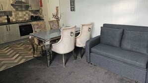 A modern kitchen with a dining area, featuring a grey sofa, a dining table with four chairs, and a decorative wall sign.