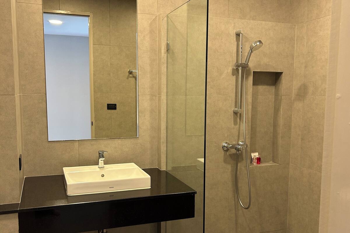 A modern bathroom with a glass shower enclosure, a black countertop sink, and a mirror above it.