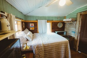 A cozy room with a bed, a small table, a lamp, and a wooden shelf with towels. - Cozy Rustic Sailors Room (Houston)