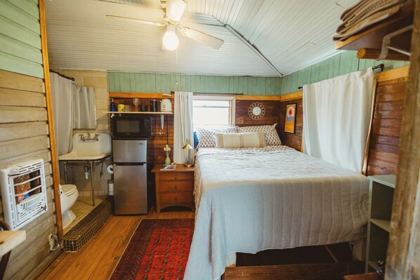 A compact bedroom with a bed, a small kitchenette, a toilet, and a ceiling fan. - Cozy Rustic Sailors Room (Houston)
