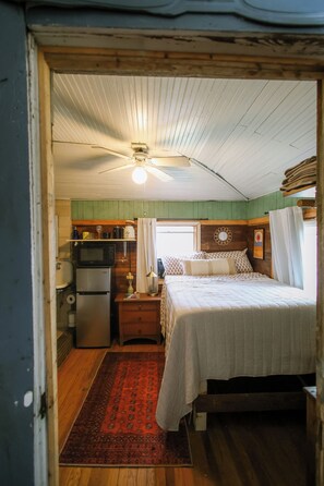 A compact room with a bed, a small kitchenette, a ceiling fan, and a red patterned rug. - Cozy Rustic Sailors Room (Houston)