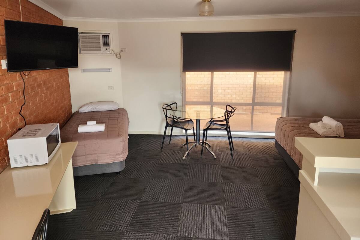 A hotel room with two beds, a TV, a microwave, a table with chairs, and a large window.