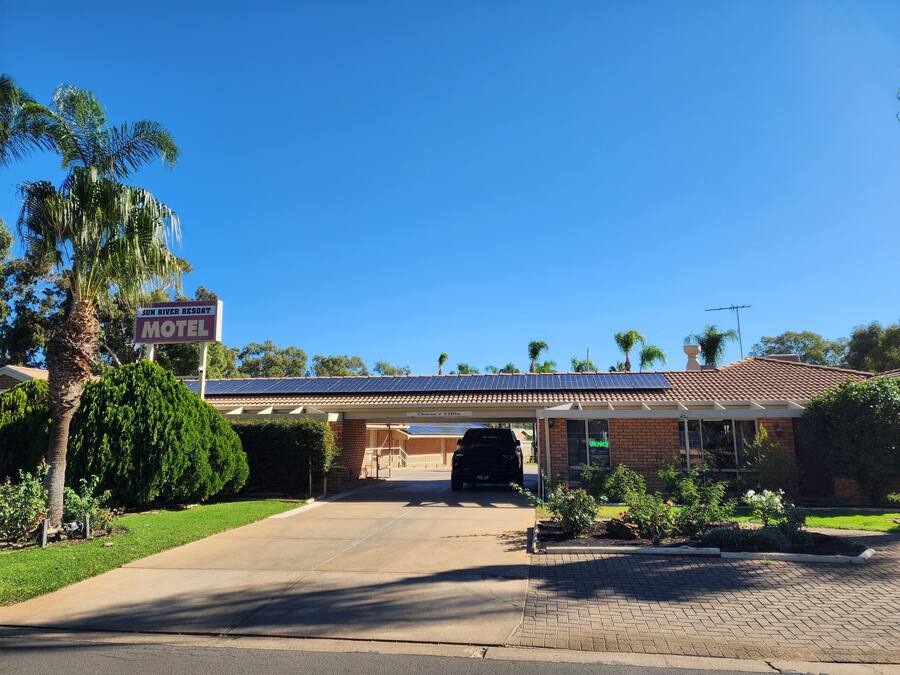 A motel with a clear sign, a covered parking area, and a brick building with solar panels.
