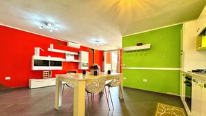 A modern kitchen with red and green walls, white cabinetry, and a dining area with a table and chairs. - "  Happy  Apartment " (Bari Sardo)