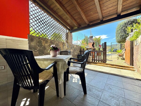 A covered patio with a table and chairs, stone walls, and a view of the backyard.