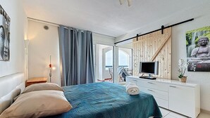 Ein Schlafzimmer mit Bett, Fernseher, Schreibtisch und Fenster mit Blick auf den Strand.