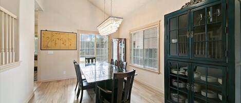 A dining room with a large table, chairs, a chandelier, and a cabinet with glass doors.