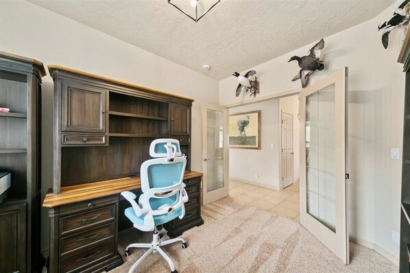 A home office with a dark wood desk, a blue office chair, and a large window. - Luxury 3 BD/3BA house in charming Boise with WiFi, AC, Bikes, Com. Pool (Boise)
