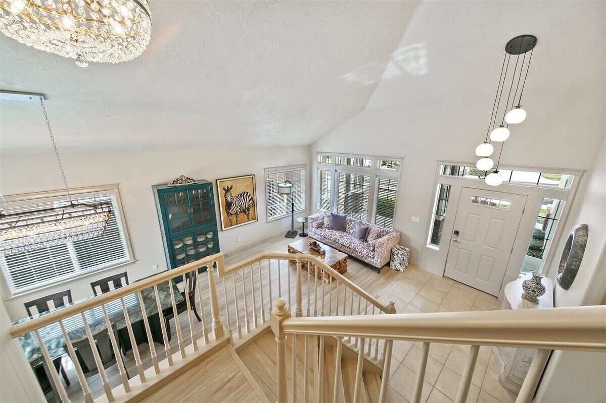 A spacious living area with a staircase, a sofa, a dining table, and a chandelier.