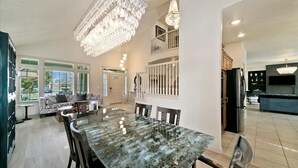 Amplia sala de estar con una mesa de comedor, un candelabro y una escalera que conduce a un nivel superior.