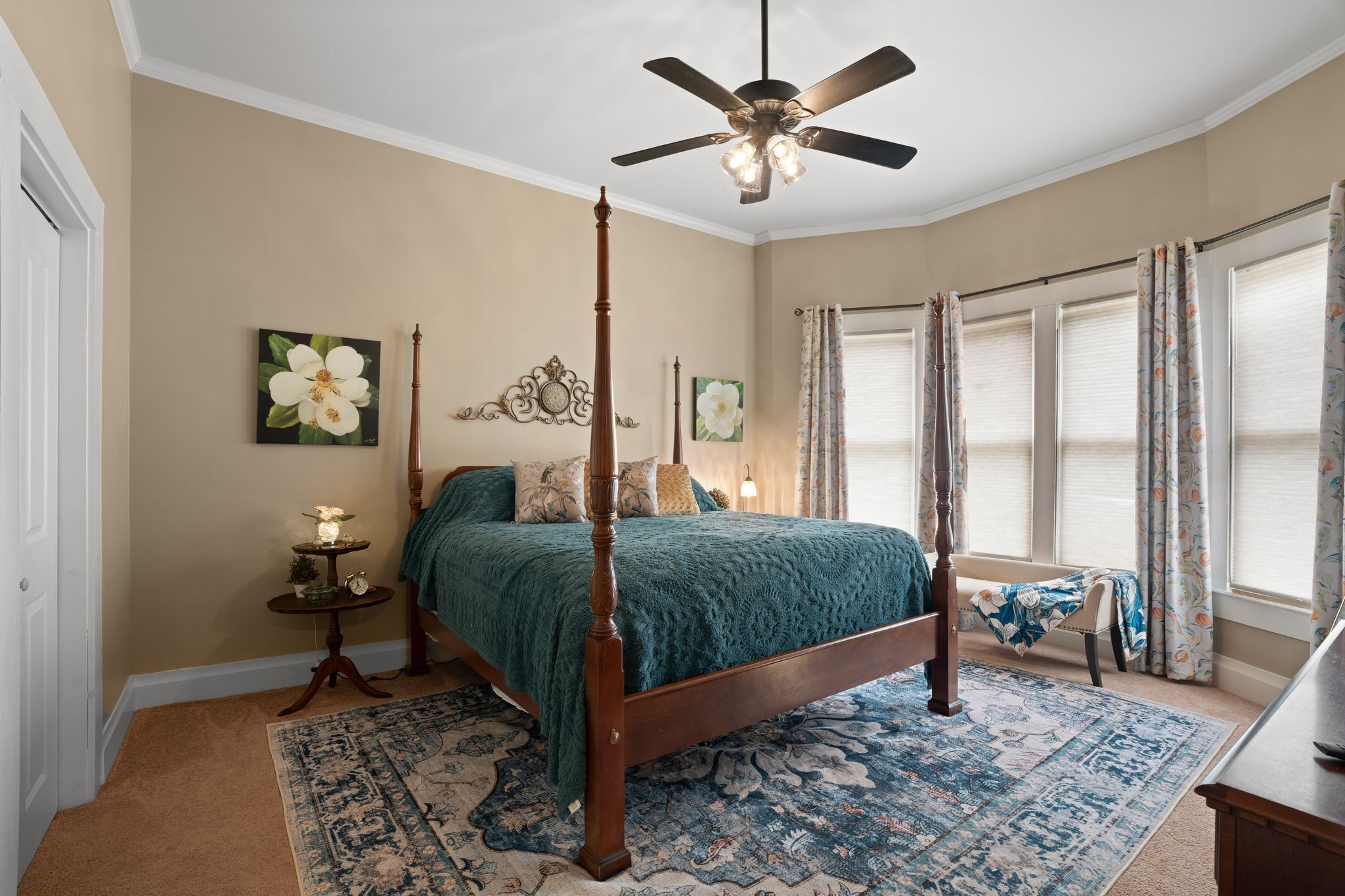 A bedroom with a four-poster bed, a ceiling fan, and a large window with curtains.