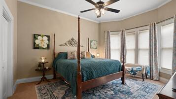 A bedroom with a four-poster bed, a ceiling fan, and a large window with curtains.