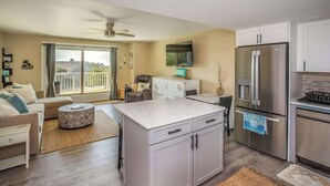 Een moderne keuken met een centraal eiland, een zithoek met een bank, een aan de muur bevestigde televisie, en een balkon met uitzicht.