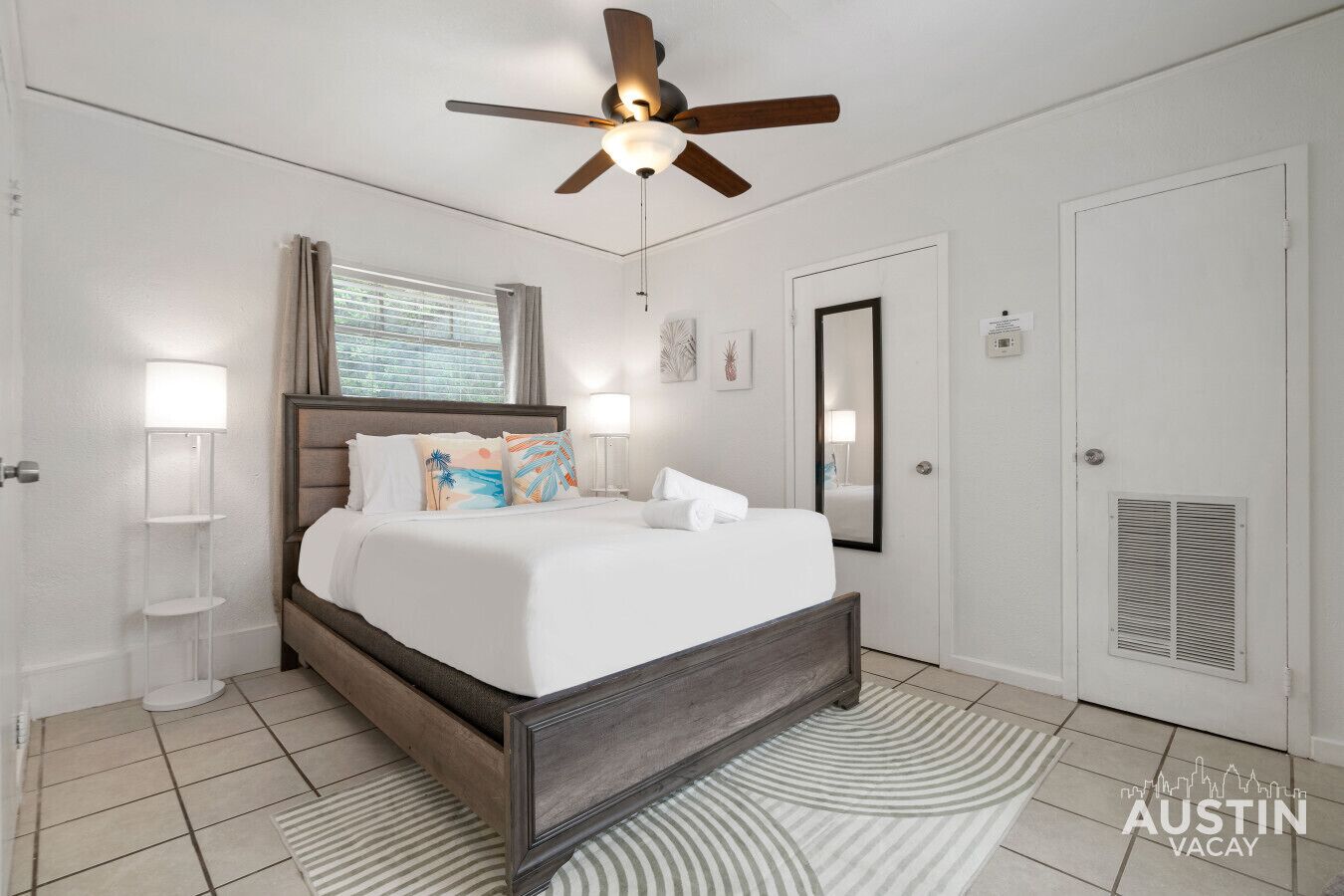 A bedroom with a bed, a ceiling fan, a window with blinds, a door, and a vent.