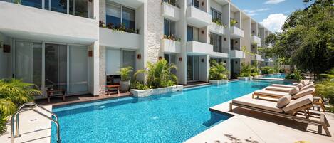 A modern hotel with a swimming pool, outdoor seating, and lush greenery.