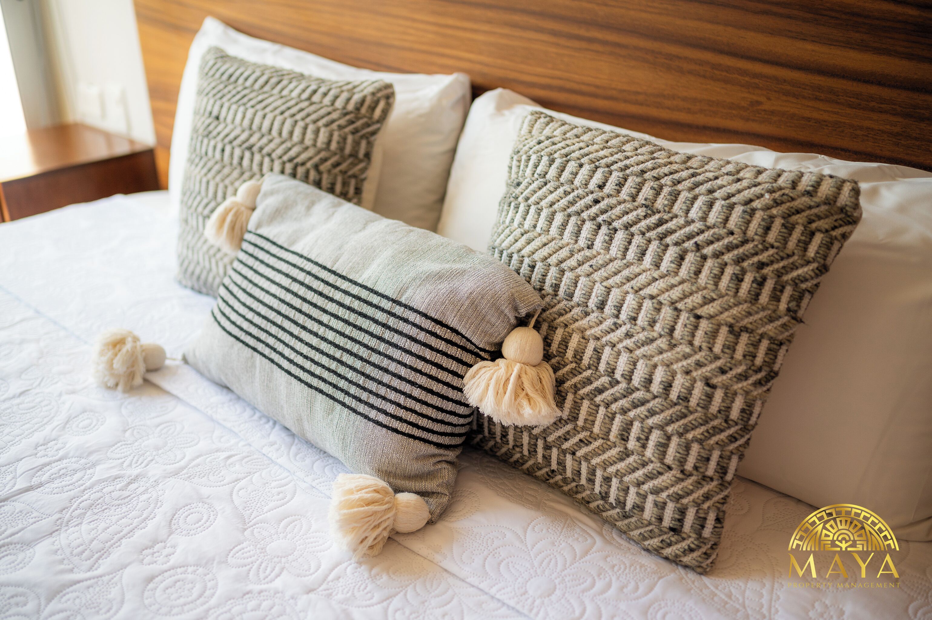 A bed with two pillows, one striped and one with a herringbone pattern, and a wooden headboard.
