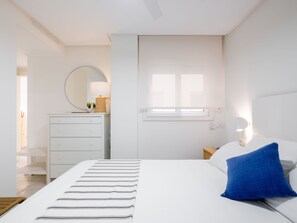 A minimalist bedroom with a bed, a bedside table, a dresser, a mirror, and a window. - Panorama by Interhome (Altea)